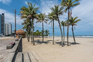 A beach with palm trees, a sandy walkway, and a building with a dome-like structure.