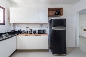 A kitchen with white cabinets, a black refrigerator, a wooden shelf, and various appliances like a coffee maker and a microwave.