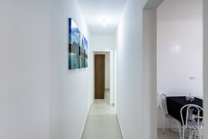 A hallway with a dining area, white walls, and a door leading to another room.