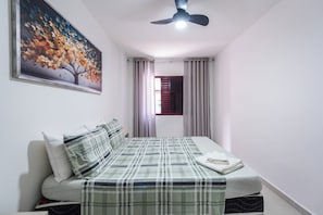 A bedroom with a bed, a ceiling fan, a window with curtains, and a wall-mounted painting.