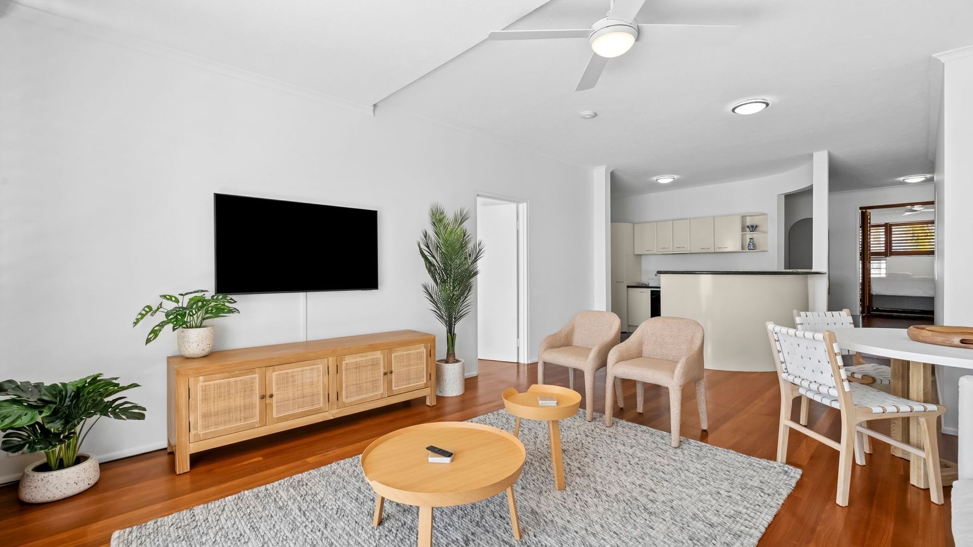 Una sala de estar moderna con un televisor de pantalla plana, muebles de madera y una cocina al fondo.