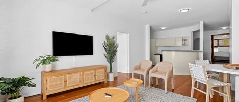 Una sala de estar moderna con un televisor de pantalla plana, muebles de madera y una cocina al fondo.