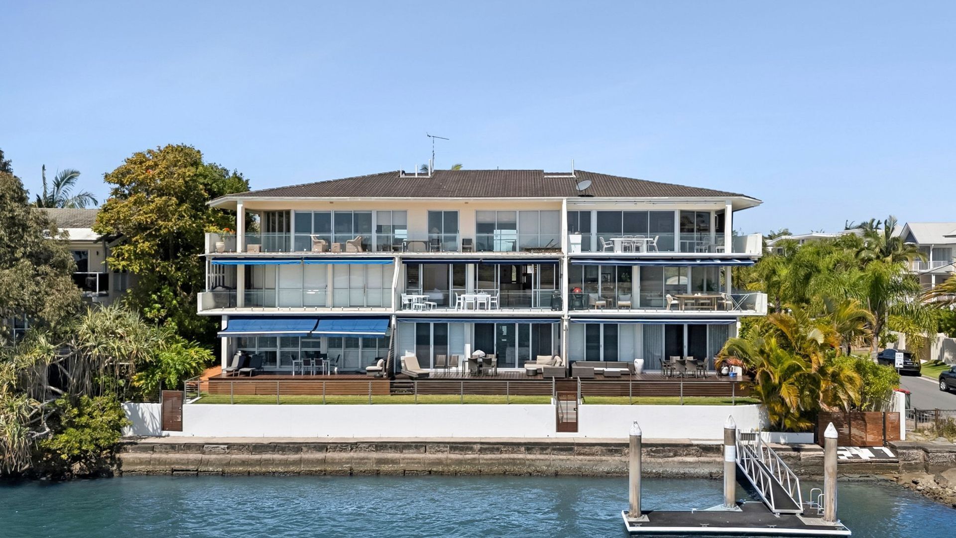 A multi-story waterfront property with balconies, outdoor seating, and a dock.