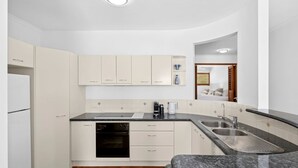 A modern kitchen with white cabinets, a built-in oven, and a granite countertop. - Mariners Point 5 Noosaville (Noosaville)