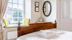 A bedroom with a large bed, a wooden dresser, a window with a view, and a mirror on the wall.