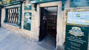 The exterior of The Original Bakewell Pudding Shop, featuring a traditional stone facade, a green awning, and signage indicating it is a historic site.
