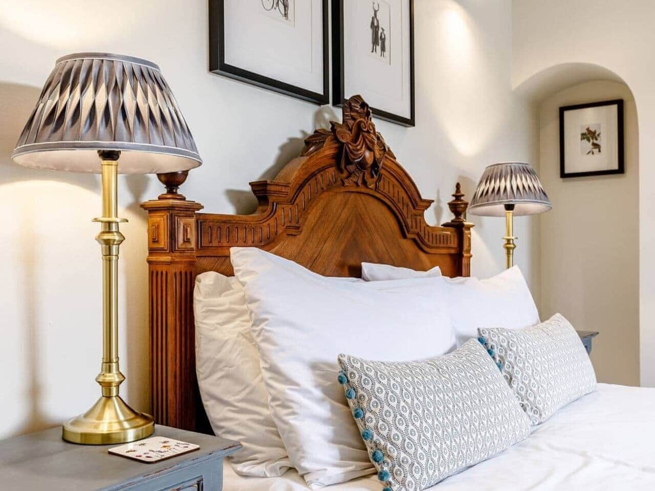 A neatly made bed with white linens and patterned pillows, flanked by two bedside lamps with lampshades.