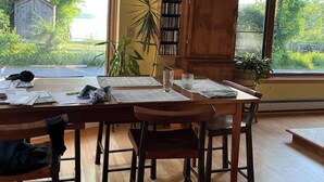 Ein Essbereich mit Holztisch, Stühlen und einer Bücherwand voller Bücher. Große Fenster bieten Blick auf Grünflächen.