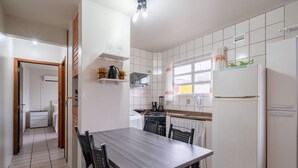 Una cocina compacta con armarios blancos, horno empotrado, refrigerador y un comedor con mesa y sillas.