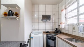 Una cocina compacta con baldosas blancas, microondas, estufa, cafetera y lavadora.