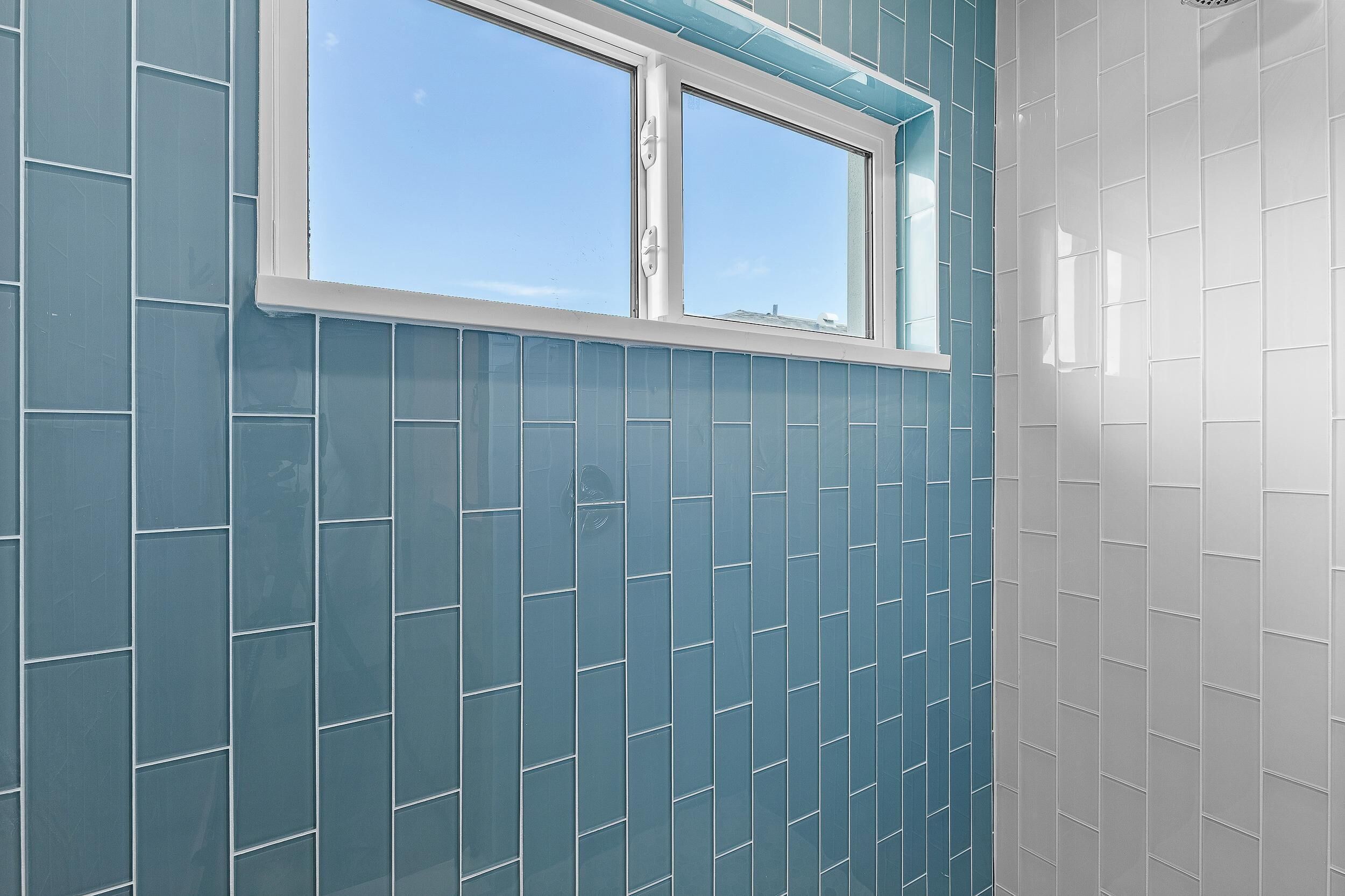 Ein Badezimmer mit blauen und weißen Fliesen, einem Fenster und einer Duschkabine.