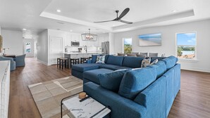 A modern living room with a sectional sofa, a dining area, and a kitchen in the background. - Flip Flop Living North (New Smyrna Beach)