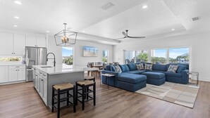 A modern kitchen with white cabinets, a stainless steel refrigerator, and a central island with stools. - Flip Flop Living North (New Smyrna Beach)