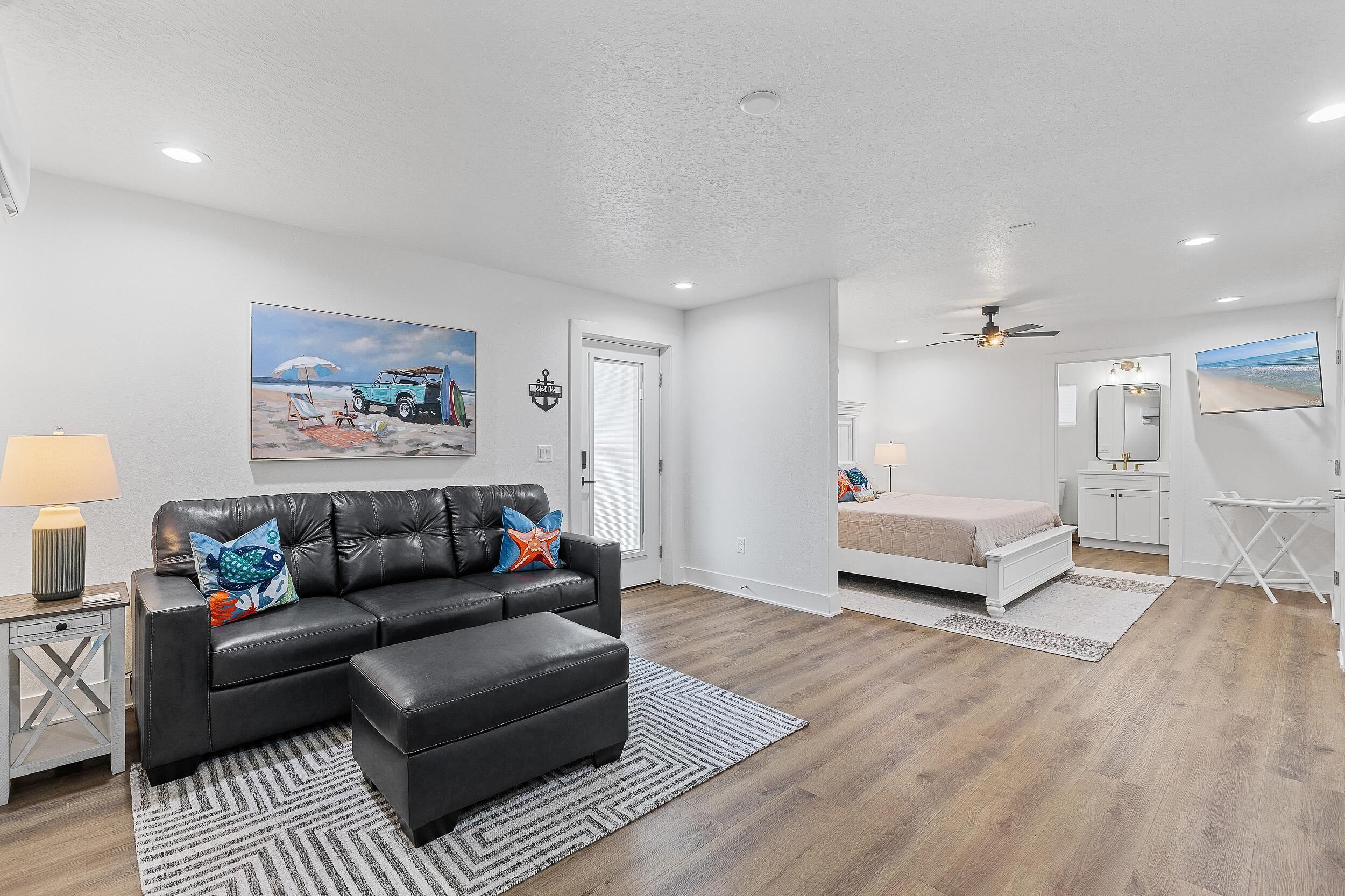 A modern living room with a black leather sofa, a matching ottoman, and a painting of a beach scene.