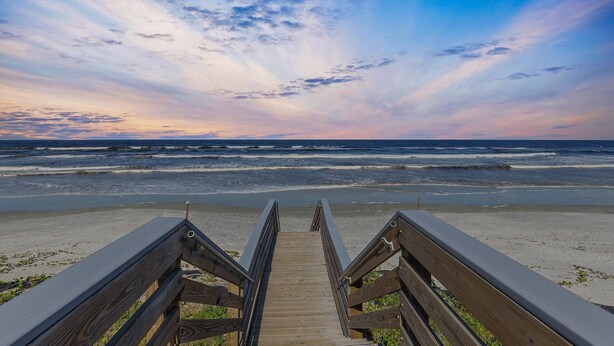 A wooden boardwalk leading to a beach with waves in the background.