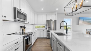 A modern kitchen with white cabinetry, stainless steel appliances, and a large island with a sink. - Flip Flop Living NSB (New Smyrna Beach)
