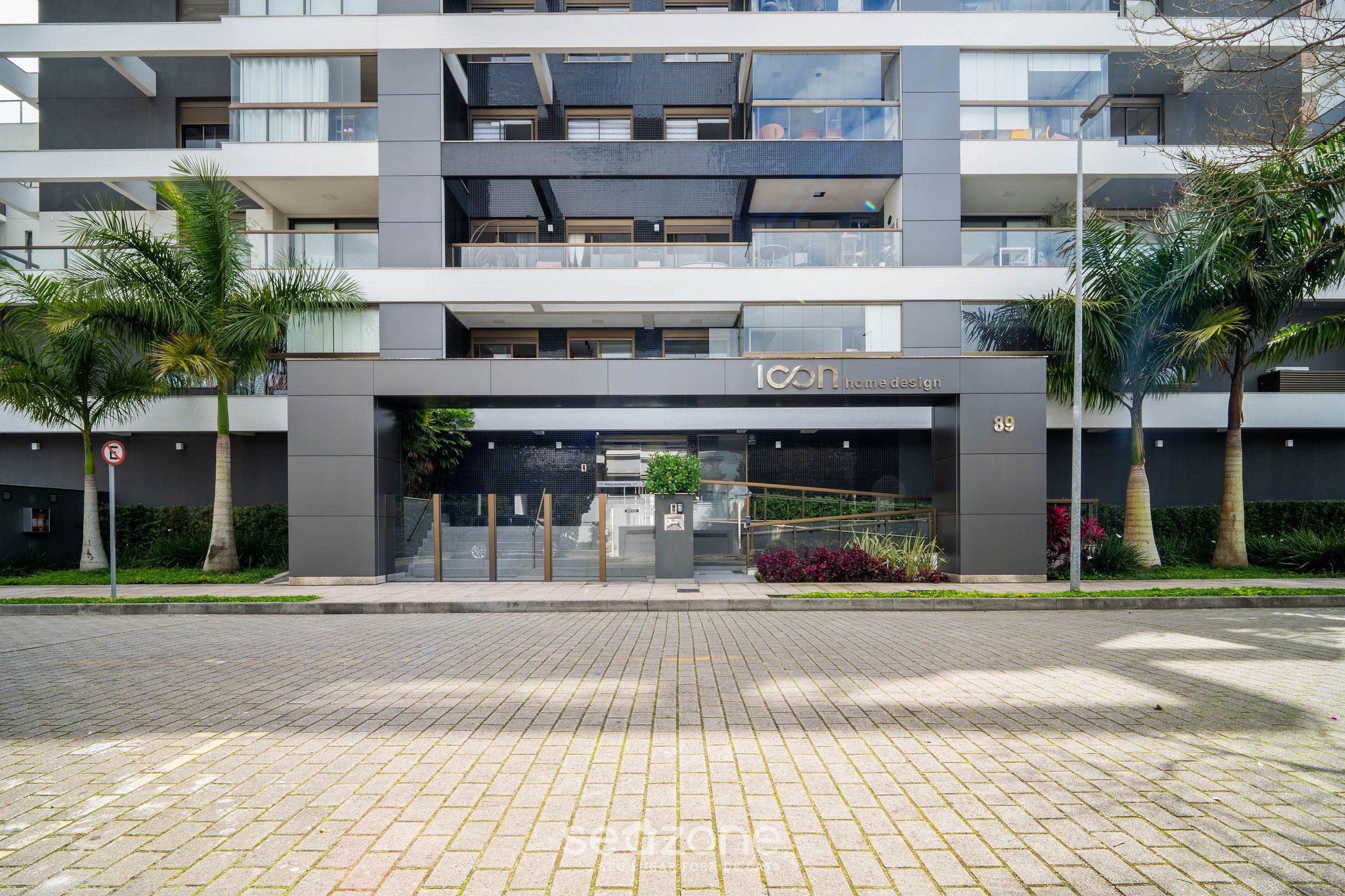 A modern multi-story building with a prominent entrance, balconies, and a well-maintained garden area.
