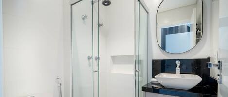 A modern bathroom with a glass-enclosed shower, a white sink with a black countertop, and a round mirror.