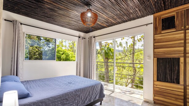 Quarto com cama, janela e porta que dá para uma varanda.