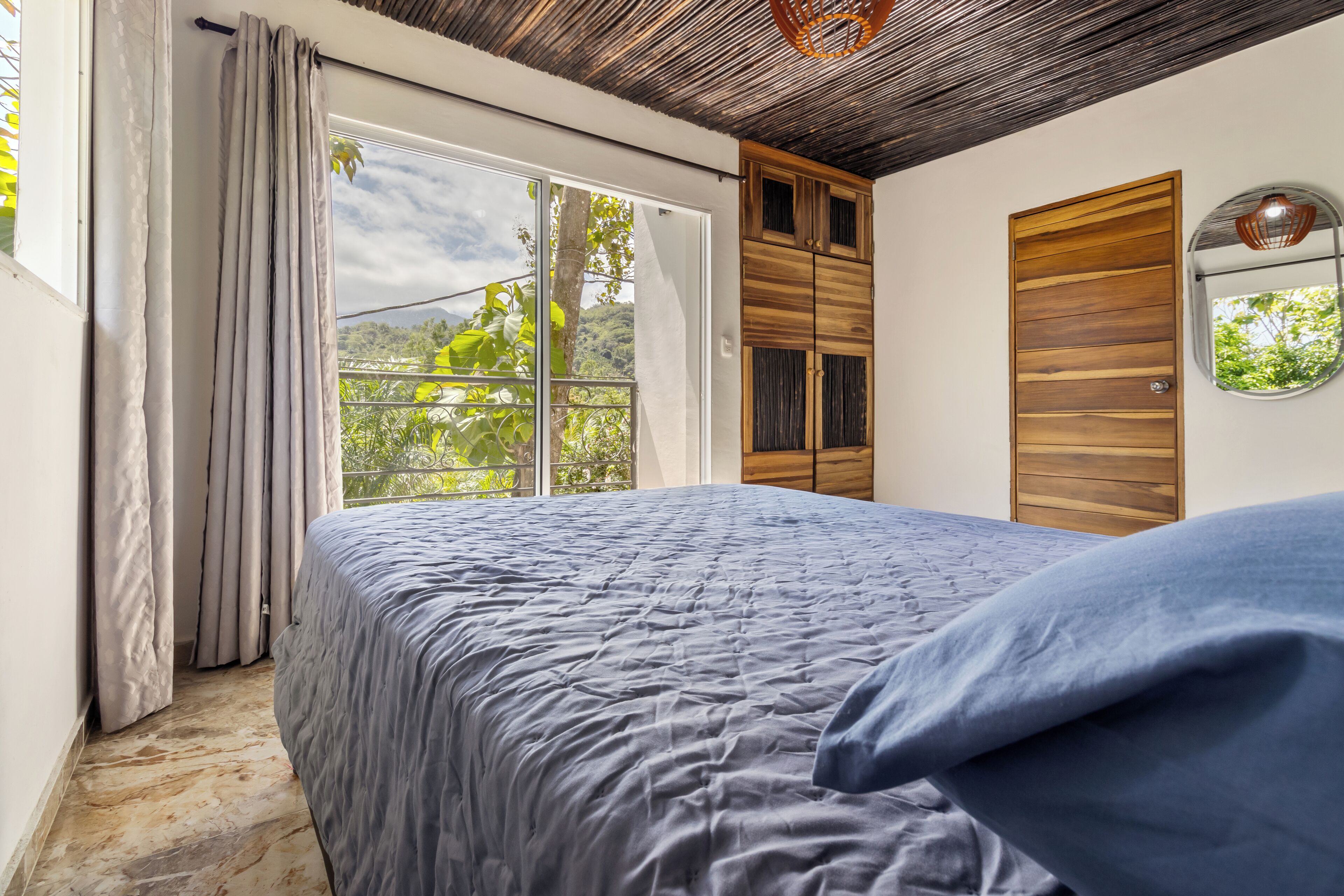 Un dormitorio con una cama grande, un armario de madera y un ventanal con vistas a zonas verdes.