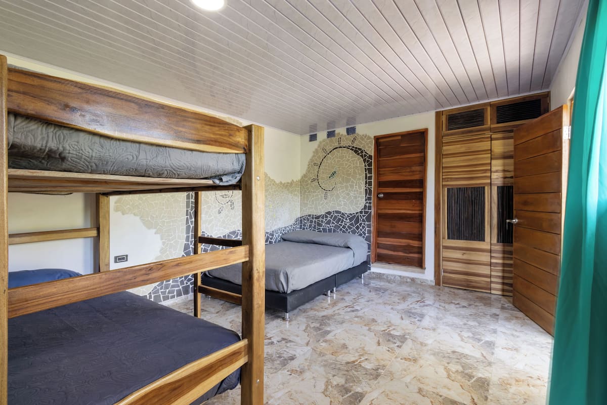 Une chambre avec des lits superposés, une armoire en bois et un mur recouvert de carreaux formant une mosaïque.