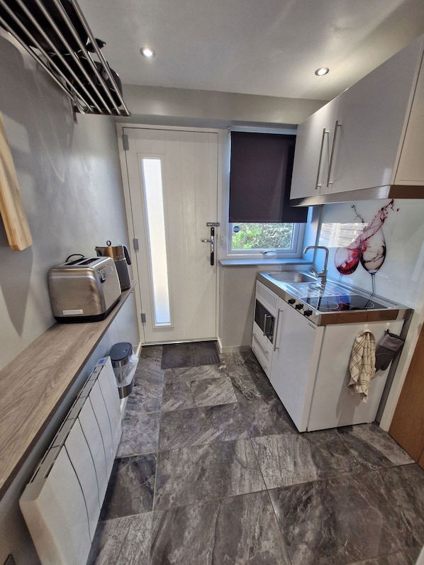 A compact kitchen with a built-in stove, a toaster, and a window with a view. - Stylish Studio Flat with Private Garden, Parking & Dog‑Friendly (Portsmouth)