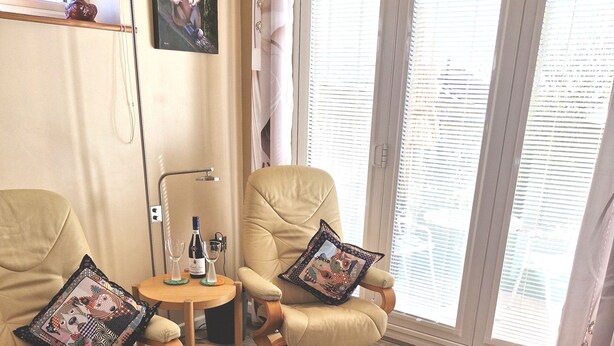 A cozy room with two beige armchairs, a small wooden table with a bottle and glass, and a round table.