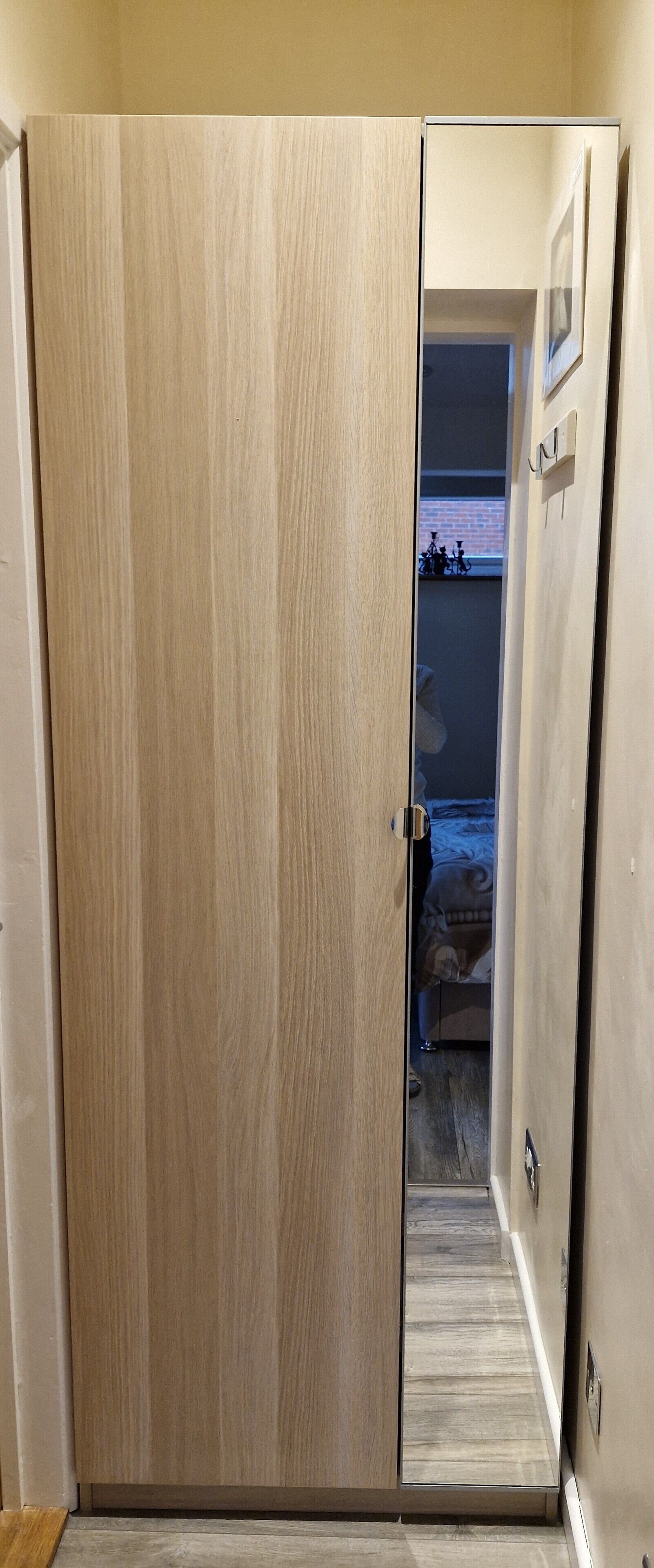 Un armario de madera con puerta corredera, un pequeño escalón que lleva a una habitación con cama y ventana.