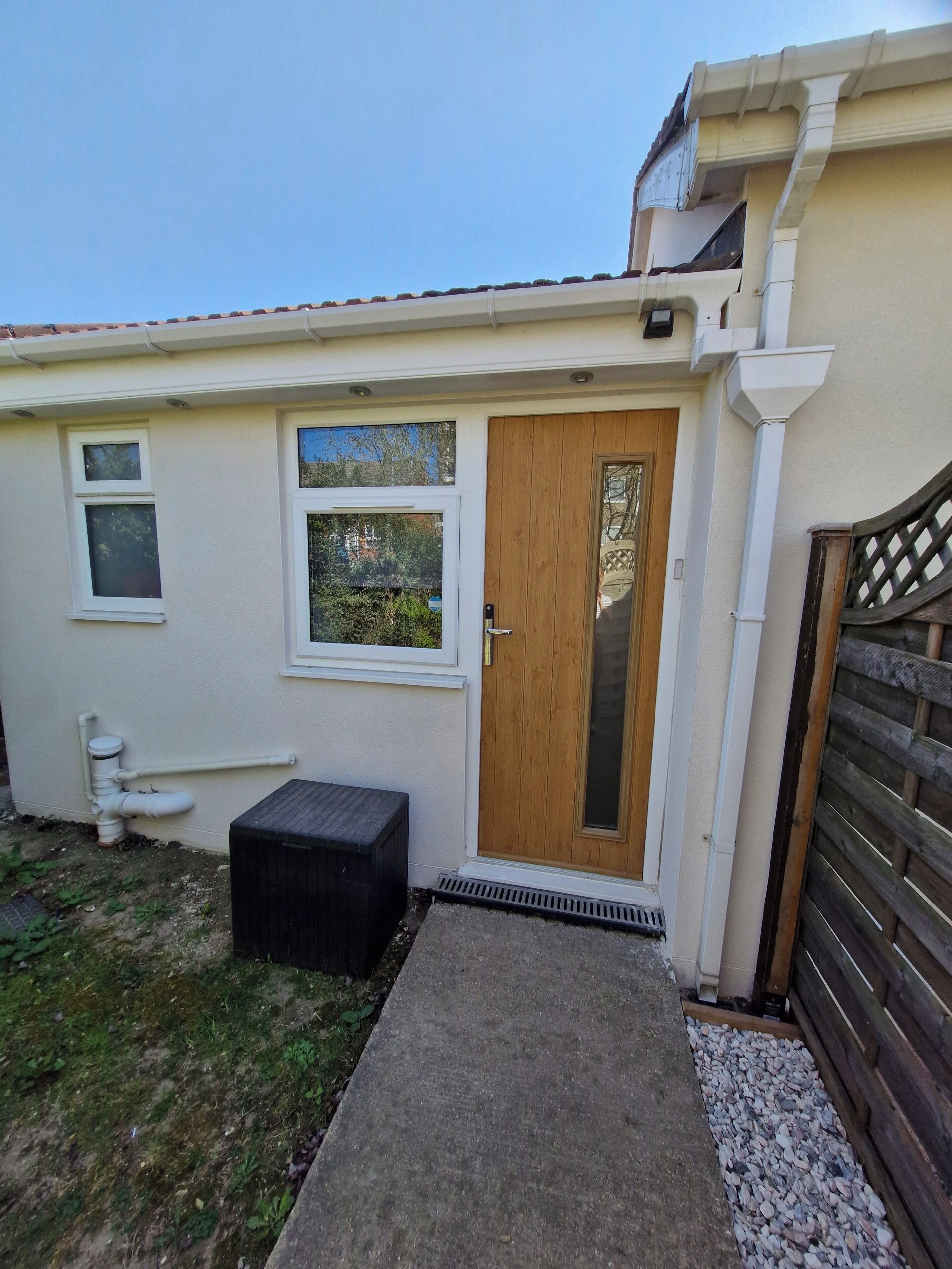 Une petite maison avec une porte en bois, une petite fenêtre et un chemin en béton menant à la porte.
