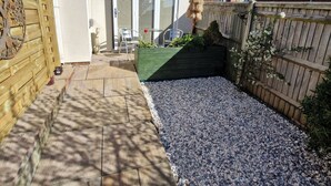 A residential backyard with a patio area, a wooden fence, and a house with a tiled roof.
