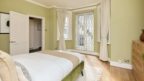 Un dormitorio con cama, ventana con cortinas, puerta y cómoda de madera.