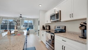 A modern kitchen with white cabinets, a granite countertop, a built-in microwave, and a coffee maker.