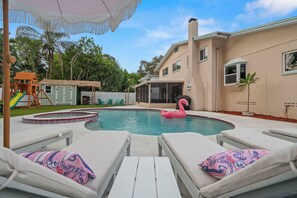 Quintal com piscina, espreguiçadeiras, boia de flamingos e casinha de brincar.