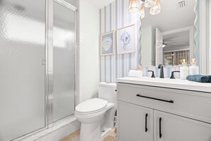 Uma casa de banho moderna com chuveiro em cabine de vidro, sanita branca, papel de parede riscado e toucador com produtos de higiene pessoal.