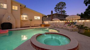 Patio trasero con piscina, jacuzzi y zona de descanso con sombrillas.