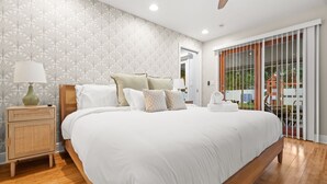 Un dormitorio con una cama grande, una mesita de noche con lámpara y vistas al exterior a través de una puerta corredera.