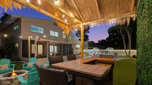Un patio al aire libre con una mesa y sillas de madera, un brasero y luces colgantes.