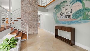 Un interior moderno con una escalera, un muro de ladrillo y un mural que da la bienvenida a The Coastal Charm.