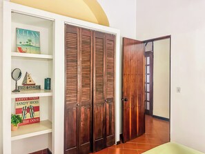 A hallway with a wooden door, a white shelf with decorative items, and a tiled floor.