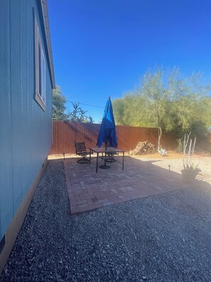 A patio area with a table and chairs, a blue umbrella, and a wooden fence.