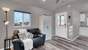 A modern living room with a leather sofa, a side table, and a floor lamp. There is a large window with a view of a house and mountains. - Central Tucson Studio Paradise (Tucson)