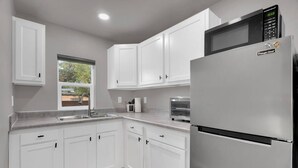 A kitchen with white cabinets, a stainless steel refrigerator, a microwave, and a window with a view of greenery outside. - Central Tucson Studio Paradise (Tucson)