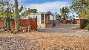 A small, rustic building with a wooden fence, a gravel driveway, and cacti in the foreground. - Central Tucson Studio Paradise (Tucson)