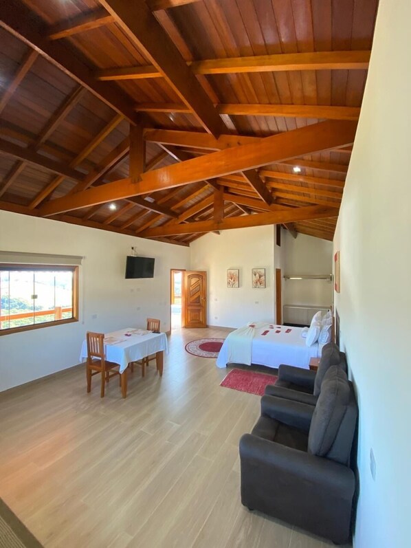 Una habitación amplia con un alto techo de madera, una zona de comedor con una mesa y sillas, una cama con un tapete rojo y un sofá.