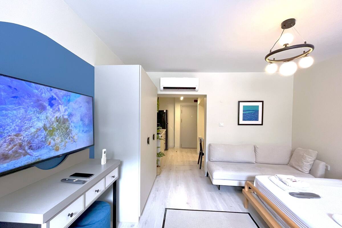 Un dormitorio moderno con cama, escritorio, televisor y un pasillo que conduce a otra habitación.