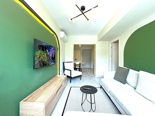 Un salon moderne avec un mur d’accent vert, un banc en bois, un canapé blanc et un téléviseur fixé au mur.