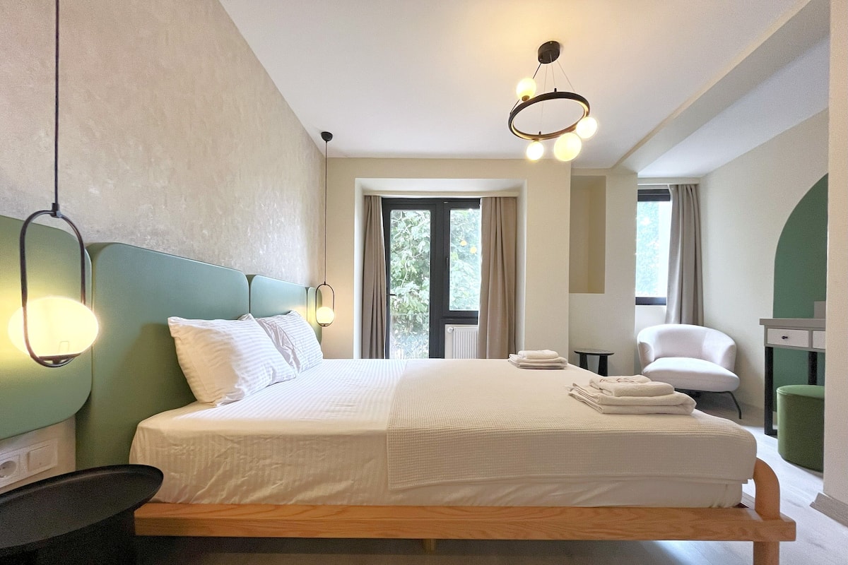 Un dormitorio moderno con una cama grande, una mesita de noche, una silla y vistas al exterior.