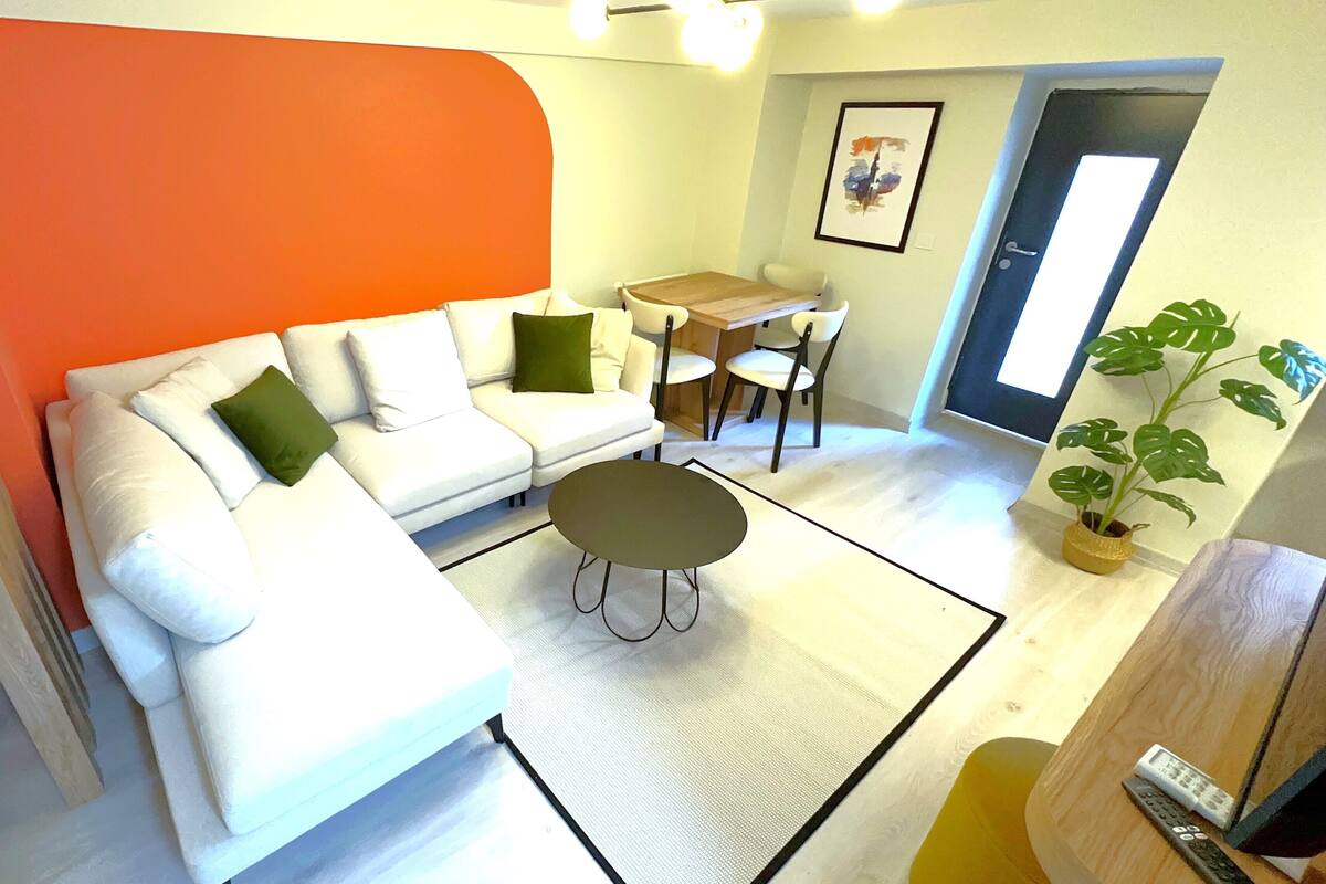 Una sala de estar con un sofá blanco, una mesita redonda y una zona de comedor con una mesa y sillas de madera.