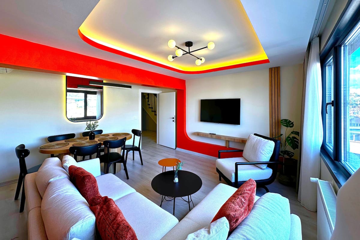 Una sala de estar moderna con un sofá, sillones, una mesa de comedor y un televisor montado en la pared.