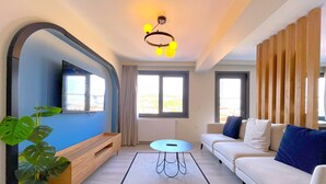 A modern living room with a sofa, a coffee table, a TV mounted on a curved wall, and a large window with curtains. - Flex Ortaköy (İstanbul)